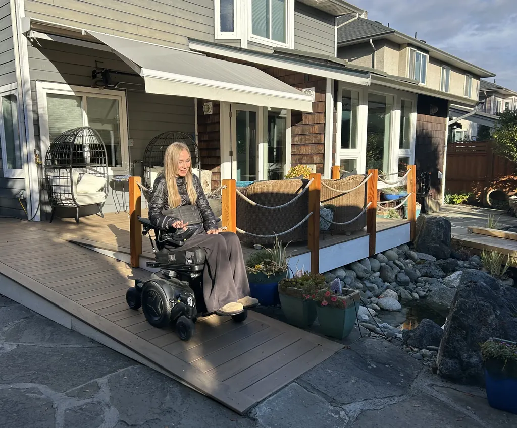 A woman in a power wheelchair drives down a wide, gently sloped composite ramp from her backyard deck.