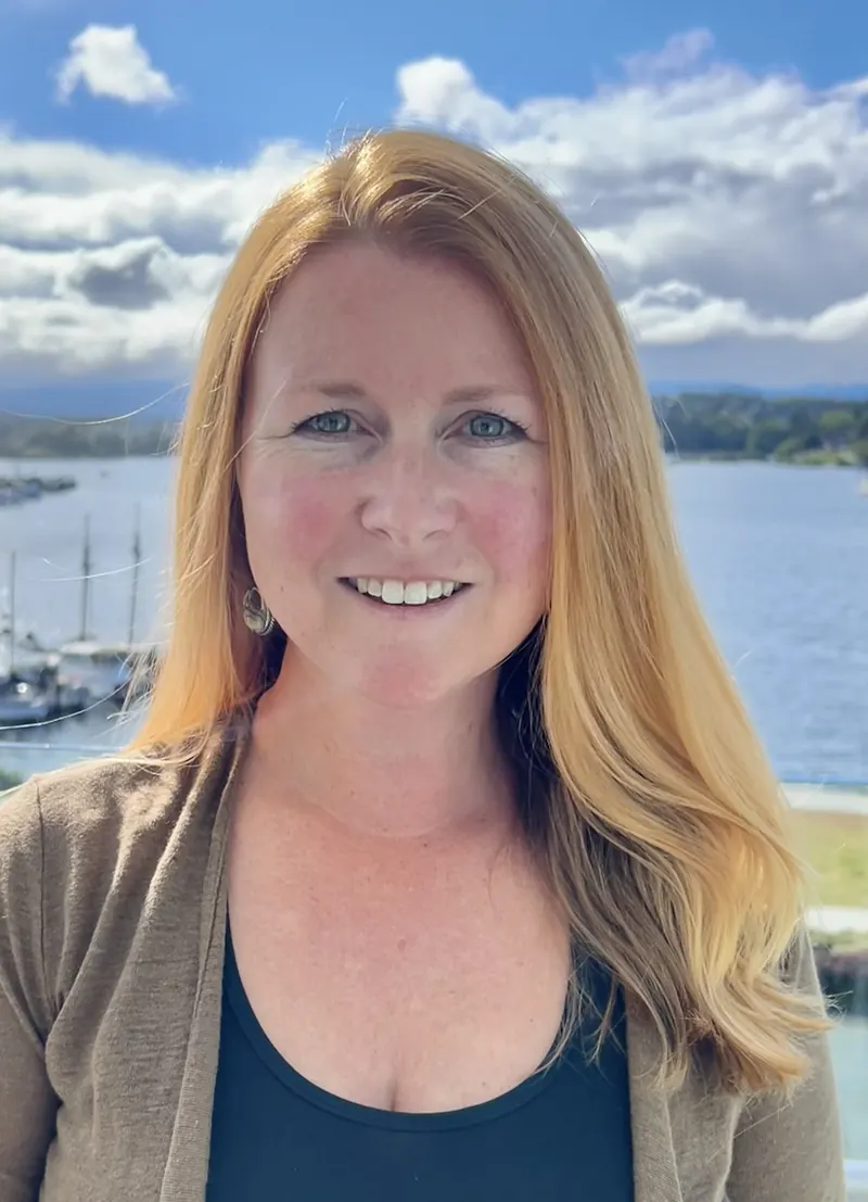 Heidi Swan, smiling, with the harbour and boats behind her.